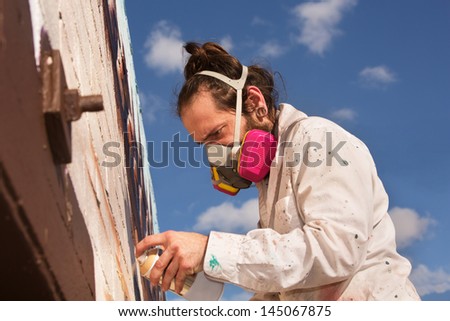 Graffiti artist with respirator spray painting a wall