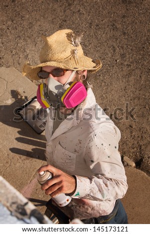 Person with hat and sunglasses spray painting a wall