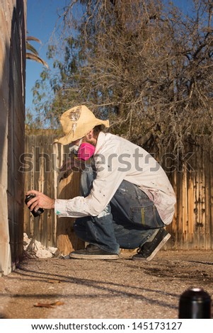 Man crouching on the ground using spray paint on a wall