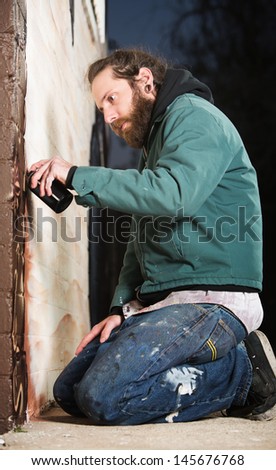 Man kneeling on the ground while spray painting a wall