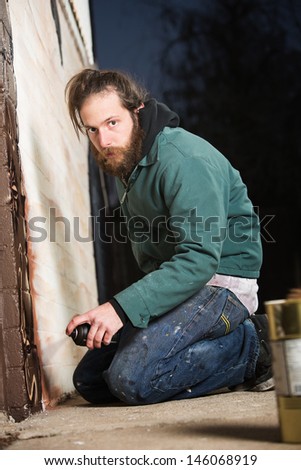 Bearded adult European graffiti artist kneeling on ground