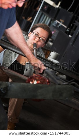 Young glass maker blowing air through tube for glass object