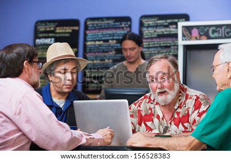 Four serious mature men in cafe with laptop