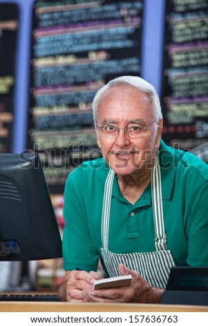 Senior man with apron behind counter taking orders