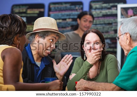 Embarrassed woman with hand on mouth with group in cafe