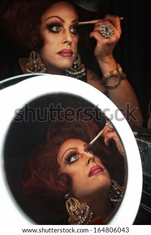 Cross dressing man putting on makeup at a mirror