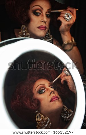 Drag queen applying makeup in front of a mirror