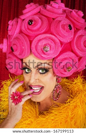 Grinning drag queen in plastic wig biting fingernails