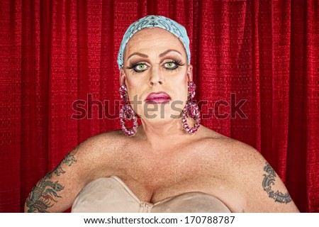 Serious cross dressing man with tattoo and curtain