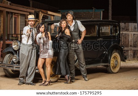 Group of 1920s vintage gangsters outside aiming weapons