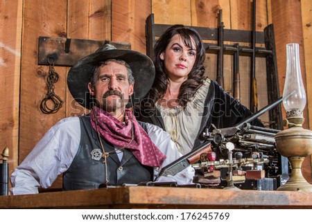 Gruff Cowboy Poses With A Rifle And Stern Saloon Girl