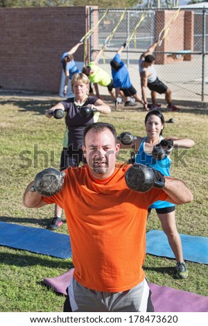 Confident man and group lifting weights in boot camp fitness class