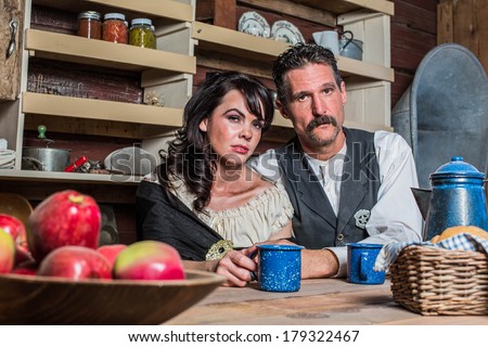 Stern looking western sheriff and woman pose inside of a house