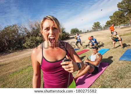 Intimidating boot camp fitness trainer with adult class outdoors