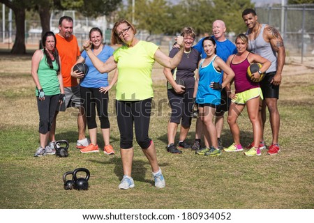 Confident mature woman flexing arms with fitness group standing