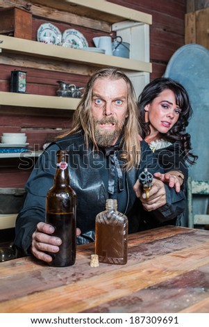 Crazed Western Man Aims Gun Towards You as he Sits at Table With Woman