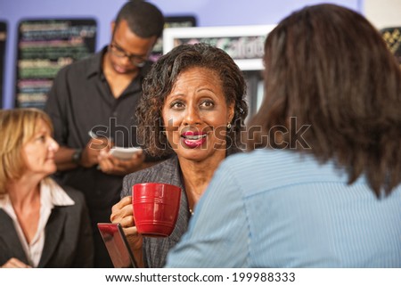 Cheerful mature woman drinking coffee with friend