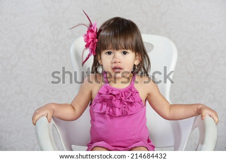 Cute toddler in chair with pink ribbon in hair