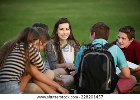 Cute female teen student studying with friends outdoors