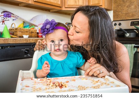 Woman in a messy kitchen kisses her baby