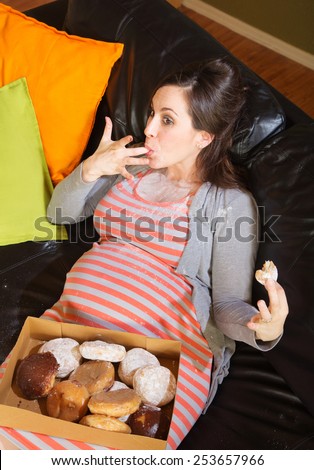 Pregnant woman with box of donuts licking her fingers