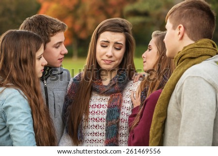 Crying teen in scarf with sympathetic friends outdoors