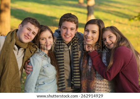Group of five cheerful youth outdoors embracing