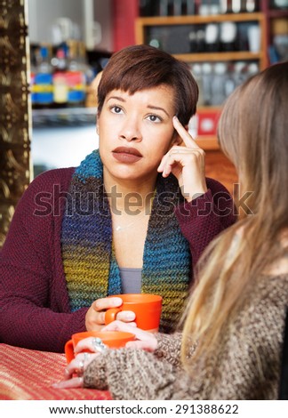Pondering woman with friend in cafe looking up