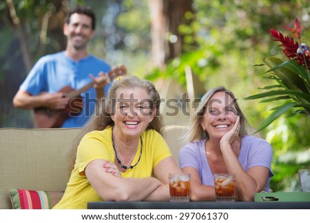 Pair of laughing female friends near ukulele player outdoors