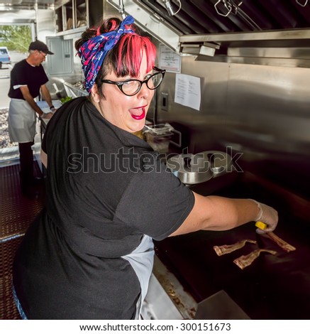 Smiling pink haired chef grills bacon in a food truck