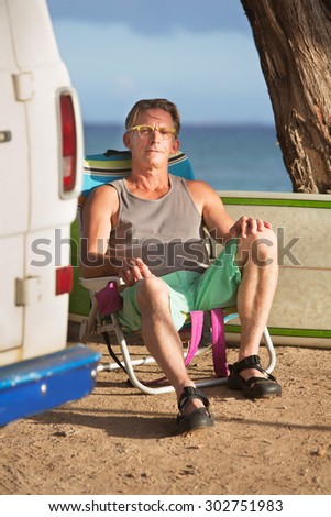 Attractive calm man sitting with surfboard behind him