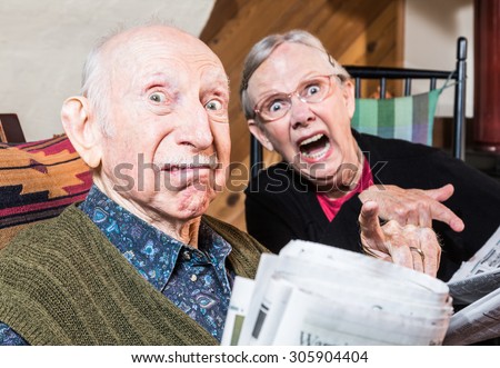 Old mad couple reading a newspaper in their living-room