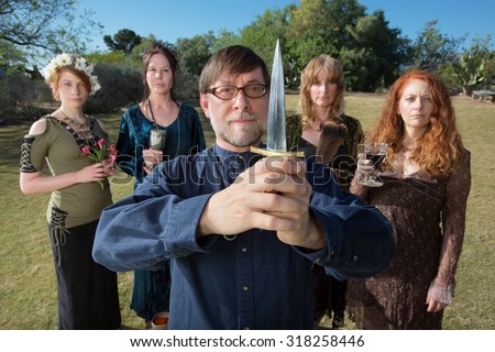 Serious male pagan priest with group and dagger outdoors