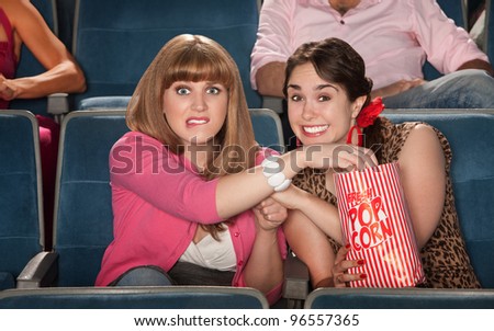 Two anxious women enjoy movie with bag of popcorn