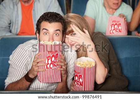 Scared couple hiding behind popcorn bags