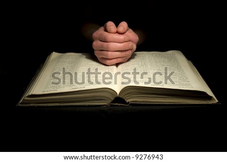 A mans hands clasped in prayer over a  Bible