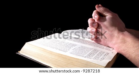 A mans hands clasped in prayer over a  Bible