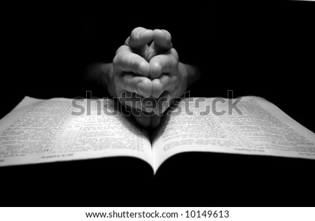 hands clasped in prayer over a  Bible