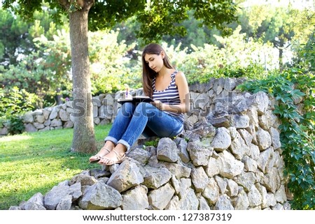 Female college student reading book carefully in park/Serious student college in a park