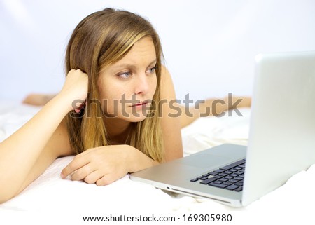 Sad woman looking computer laying in bed