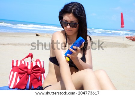Beautiful brunette with sun cream on her arm on beach