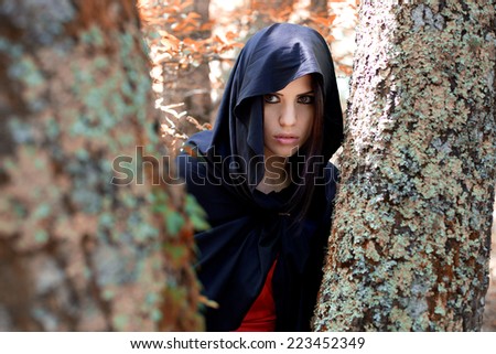 beautiful young woman hidden among the trees looking at something. Fantasy woods