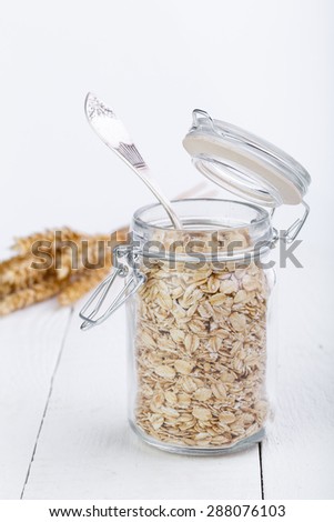 The oat flakes in jar and wheat on wooden table.