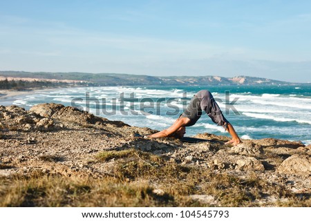 Young woman doing yoga on a rocky seashore. Doing downward facing dog pose
