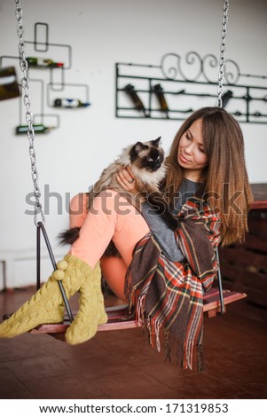 Pretty young woman with siamese cat in  warm wool socks with plaid sitting on a swing at home