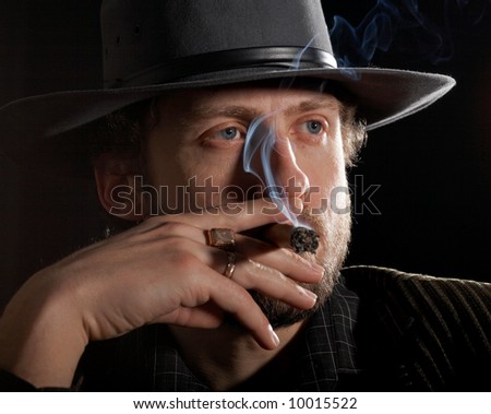 A bearded man in a hat taking a drag on his cigar