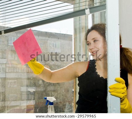 A picture  of a  young  pretty  woman in  yellow gloves doing her housework - cleaning a window with a red  rag