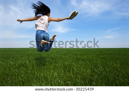 A woman is making a happy jump on a green field