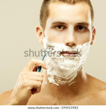 young man shaving in the bath. He is passing the razor for the beard while it looks at the mirror