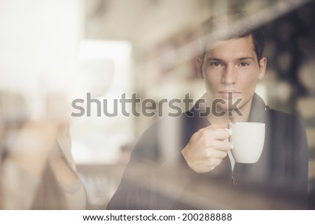 Thoughtful adult man with coffee cup looking through window in cafe